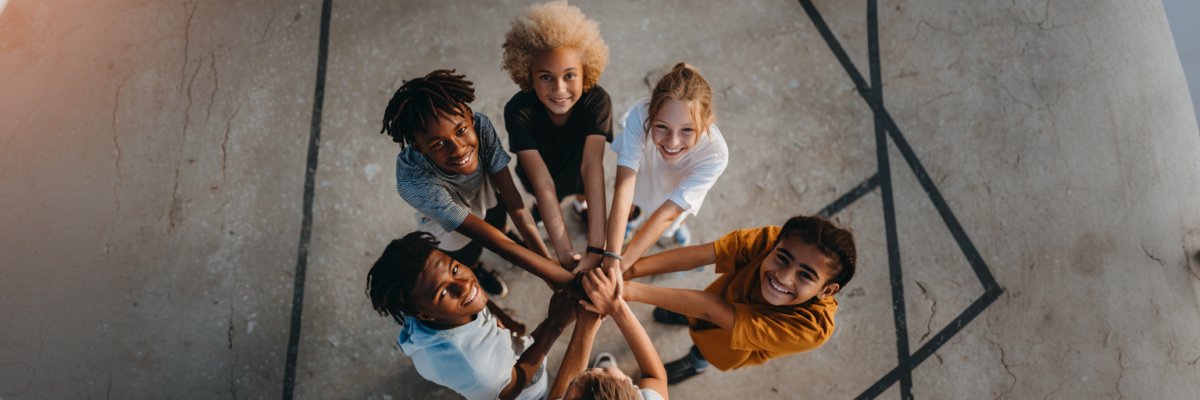 Gruppe von sechs Jugendlichen steht im Kreis und legt ihre Hände übereinander