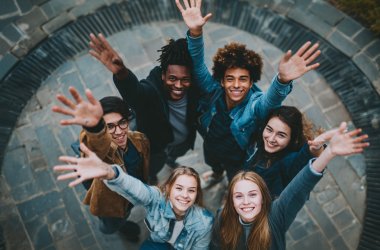 Gruppe von fünf Jugendlichen steht im Kreis auf gepflastertem Boden und streckt die Hände nach oben.