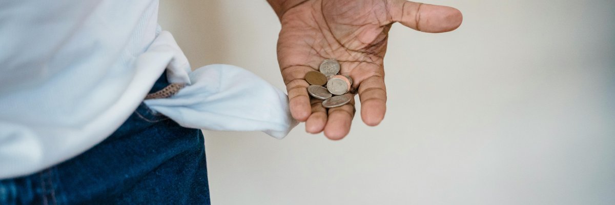 Foto: Eine nach außen gestülpte, leere Hosentasche und eine offene Hand mit Kleingeld.