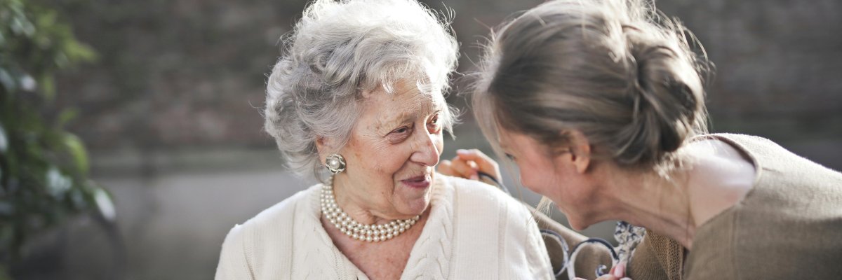 Foto: Eine jüngere Frau beugt sich zu einer älteren Frau und hört ihr zu.