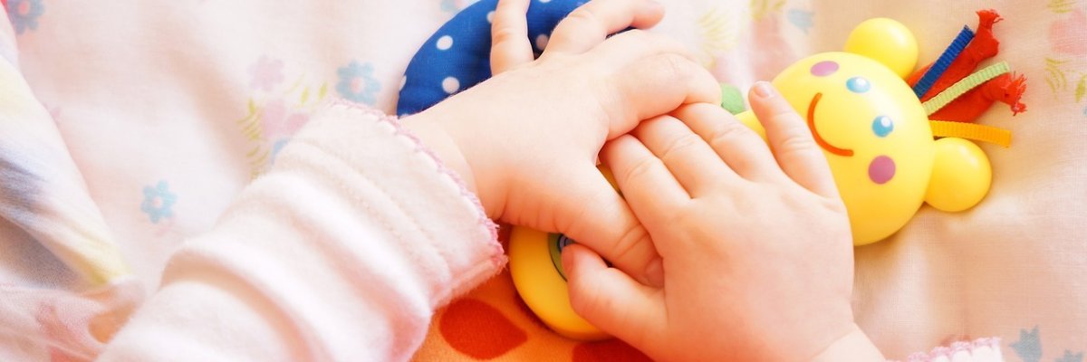 Foto: Hände eines Babys, die ein Spielzeug halten.