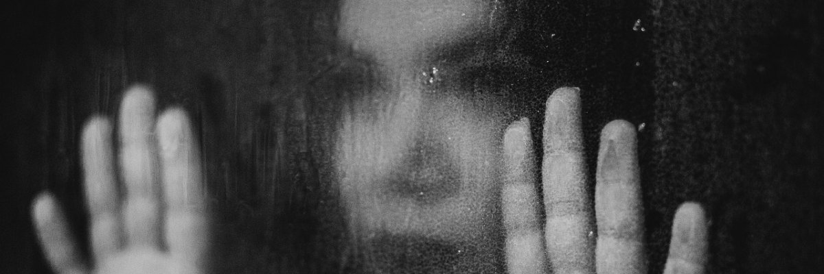 Foto: Eine Frau schaut durch eine Glasscheibe und hält beide Hände an die Scheibe.