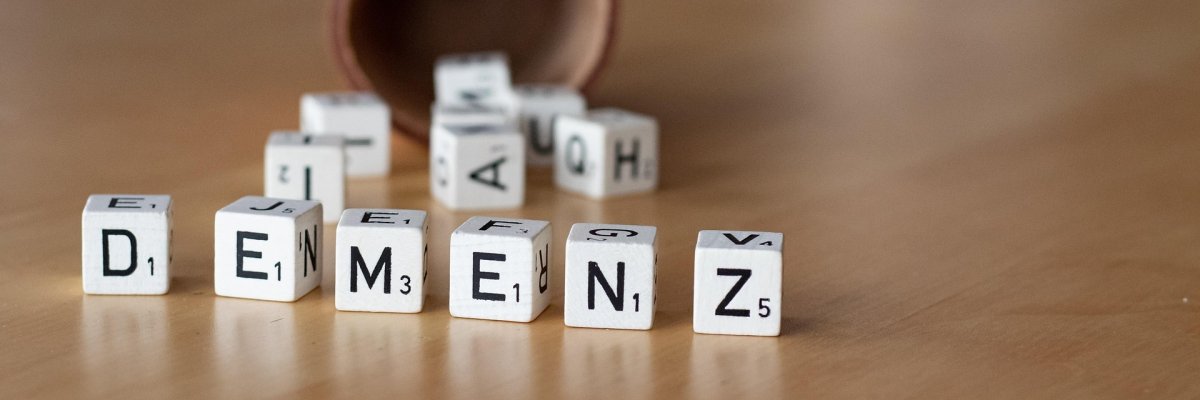 Foto: Liegender Würfel, davor liegen Buchstabenwürfel, die das Wort Demenz bilden.