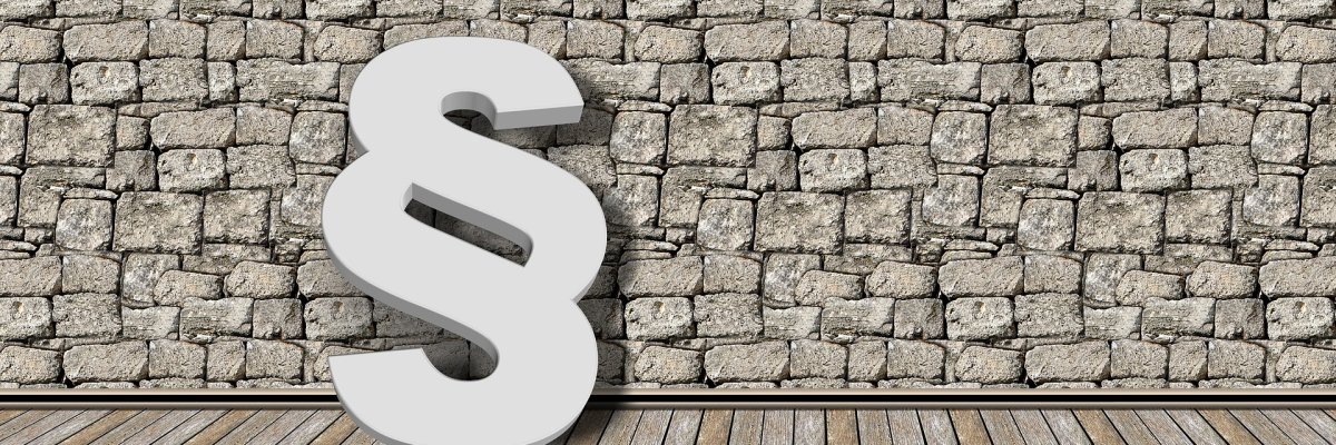 Foto: Steinmauer an der ein großes Paragrafenzeichen lehnt.