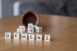 Foto: Würfelbecher vor dem Würfel mit den Buchstaben des Wortes Demenz liegen.