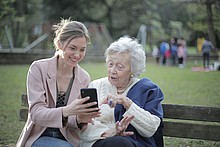 Eine junge Frau zeigt einer alten Dame etwas auf ihrem Handy.