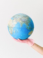 Foto: Globus der von einer Hand mit Latexhandschuh gehalten wird.