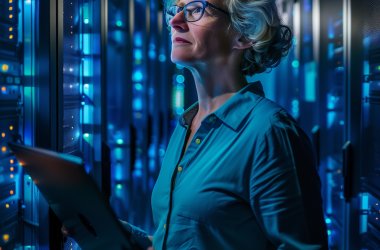 Frau mit Brille steht in einem Serverraum, hält ein Tablet und betrachtet konzentriert leuchtende Serverracks. (KI-generiert)