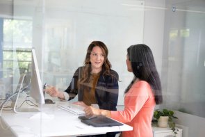 Zwei Frauen stehen am Stehtisch vor dem Bildschirm und reden miteinander über fachliche Themen
