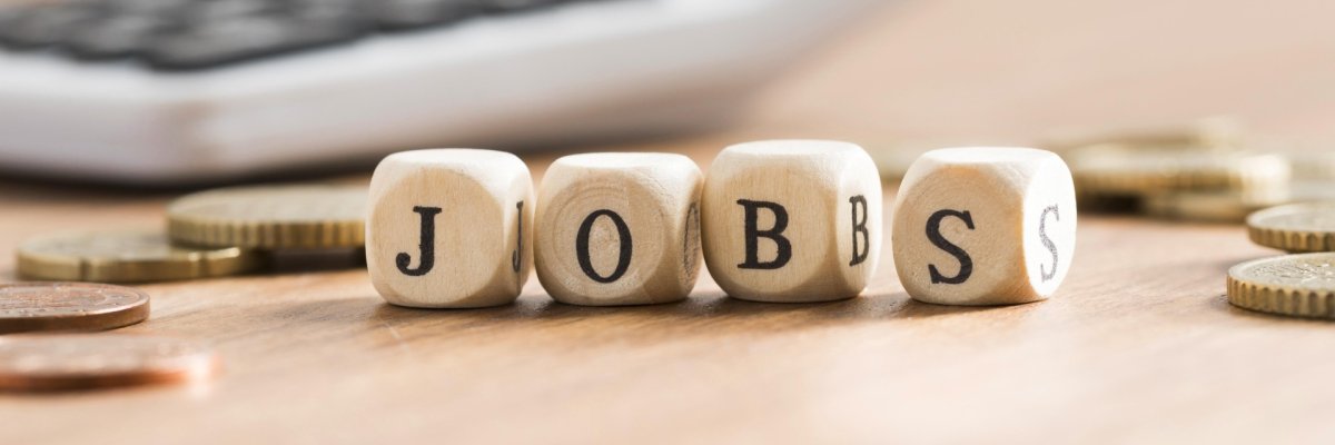 Vier Würfel liegen auf dem Tisch und zeigen zusammengesetzt das Wort JOBS.