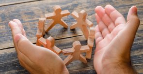 Business success concept on wooden background high angle view. hands protecting wooden figures of people.