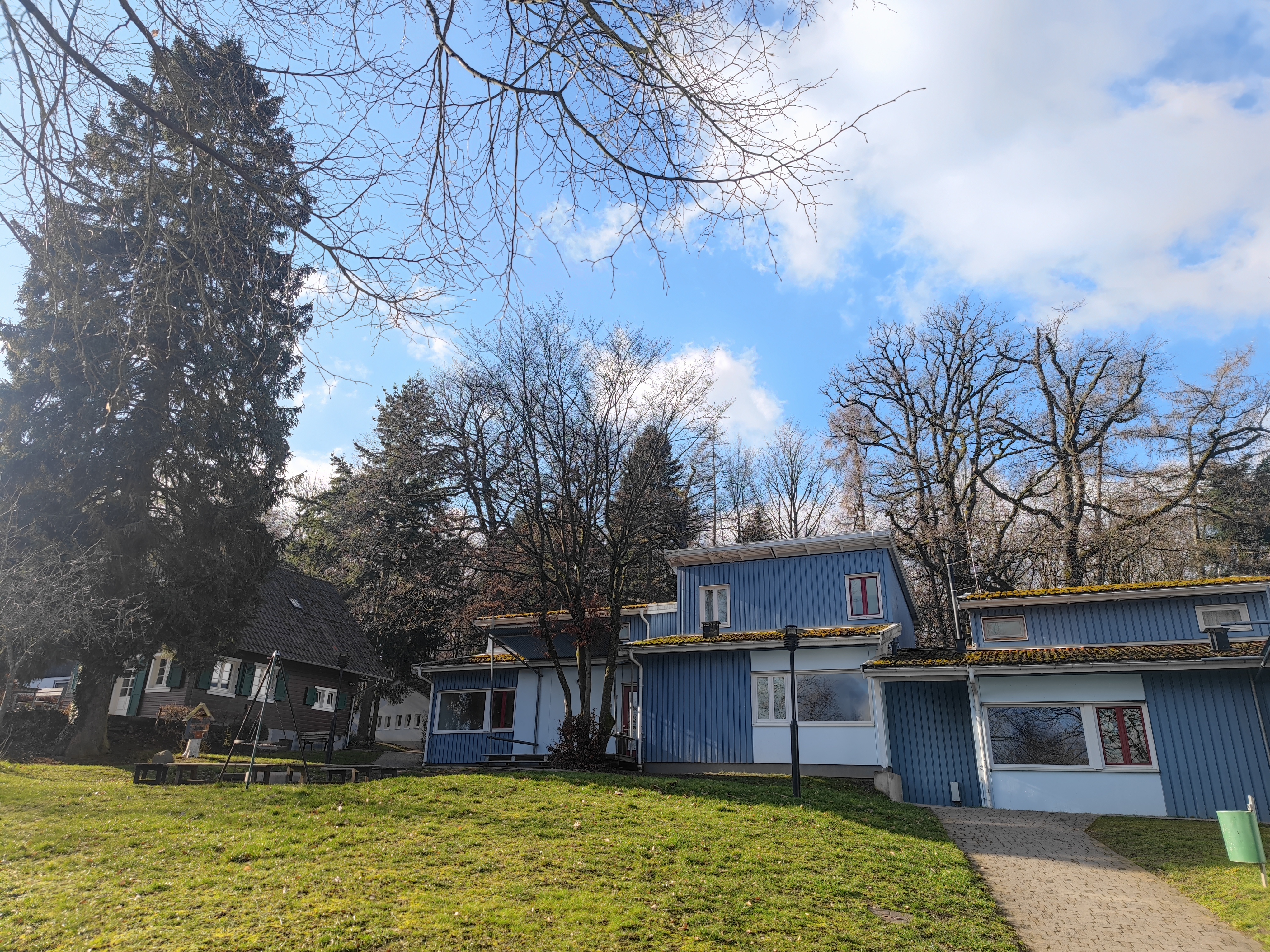 Blau-weiß gestrichene Häuser mit mehreren Fenstern, umgeben von Bäumen und einer Wiese im Vordergrund.