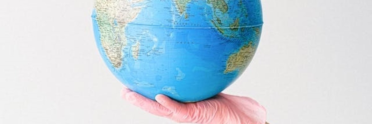 Foto: Eine Weltkugel liegt auf einer Hand mit Hygienehandschuh