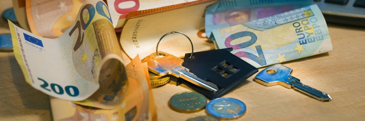 Foto Wohngeld Foto: Auf einer Tischplatte liegen ein Wohnungsschlüssel, Geld und ein Taschenrechner.