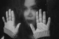 Foto Suchtberatung Foto: Eine Frau schaut durch eine Glasscheibe und hält beide Hände an die Scheibe.