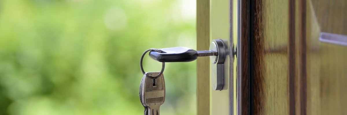 Wohnungsnotfallhilfe Foto: Geöffnete Haustür, in deren Schloss ein Schlüssel steckt.