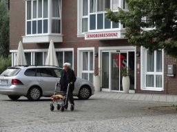 Foto: Eingang eines Seniorenheims. Davor ein alter Mann mit Rollator.