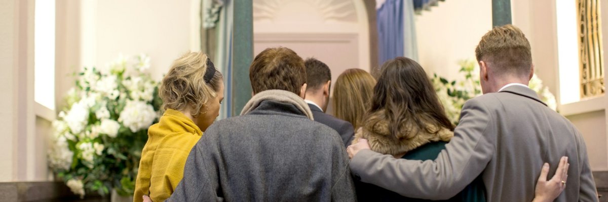 Bestattungskosten Foto: Rückenansicht von trauernden Menschen, die sich gegenseitig Halt geben.