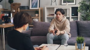 Foto: Auf einem Sofa sitzender Jugendlicher, der mit einer Frau spricht.