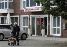 Symbol: Haus mit Senioren, die von Händen beschützt werden.