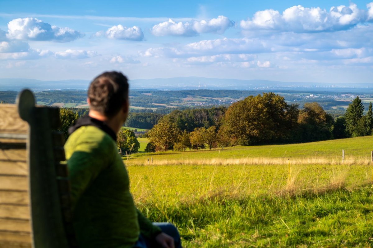 (c) André Schösser Ausblick von Neunkirchen (Modautal) Wanderer sitzt auf einer Bank in Neunkirchen und genießt den Ausblick bis nach Frankfurt am Main