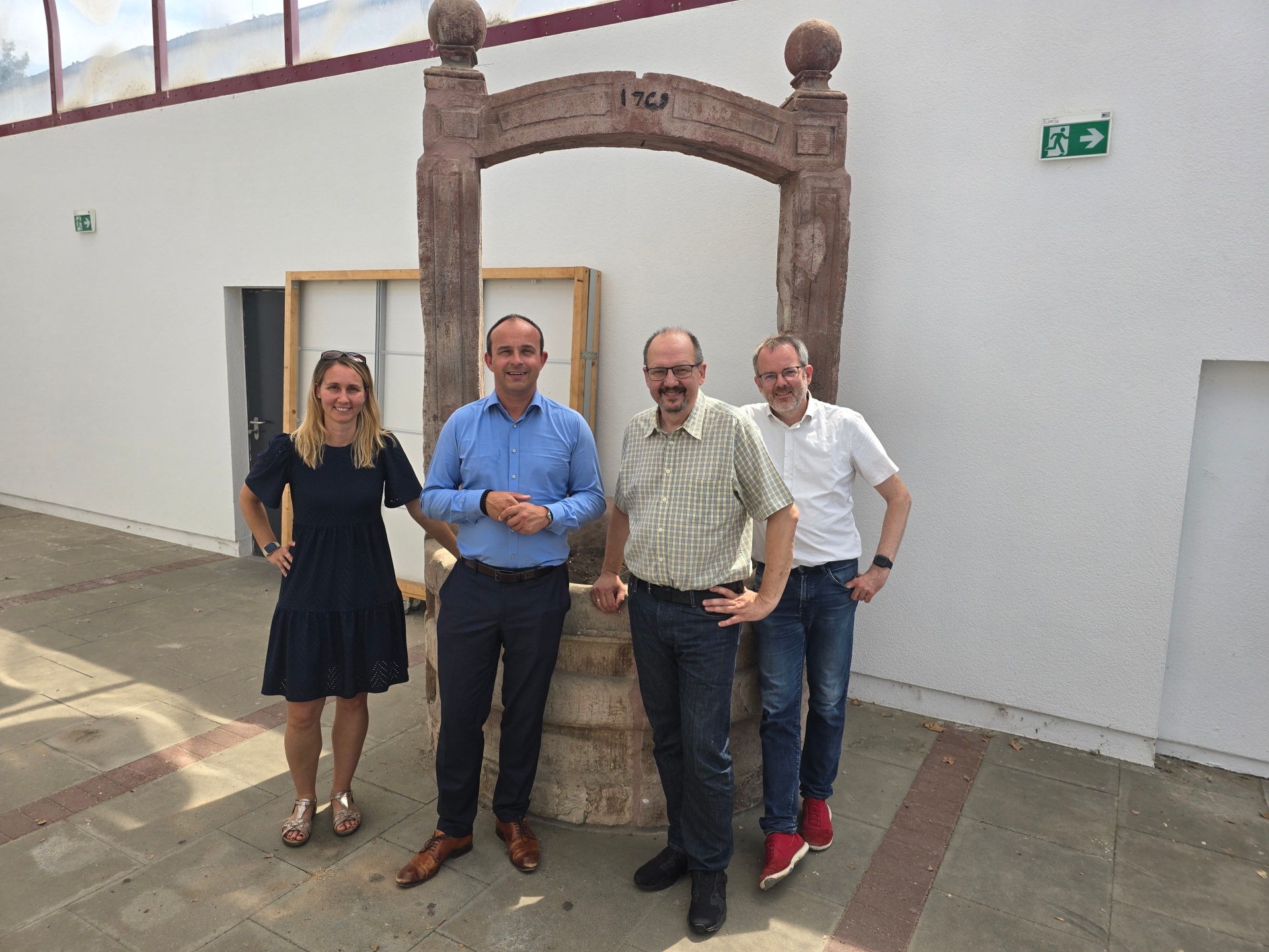 Schulleiterin Lenka Hertel, Vize-Landrat Lutz Köhler, Bürgermeister Markus Hennemann und Bickenbachs Erster Beigeordneter Tim Schmöker vor dem Sandsteinbrunnen, der in die neue Halle mit Bibliothek integriert wird