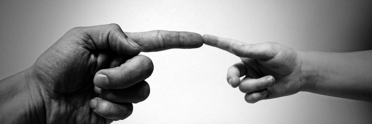 Schwarz-Weiß-Aufnahme, die zeigt, wie sich die Zeigefinger einer größeren, erwachsenen Hand und einer kleineren Kinderhand sanft berühren und die Schaffung einer neuen, unterstützenden Verbindung symbolisiert.